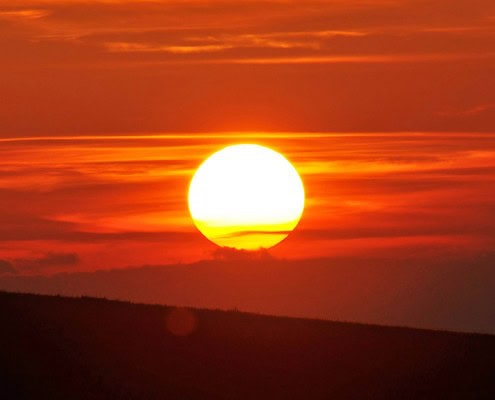 Vibrant sunset with a glowing sun over rolling hills, showcasing natural beauty.