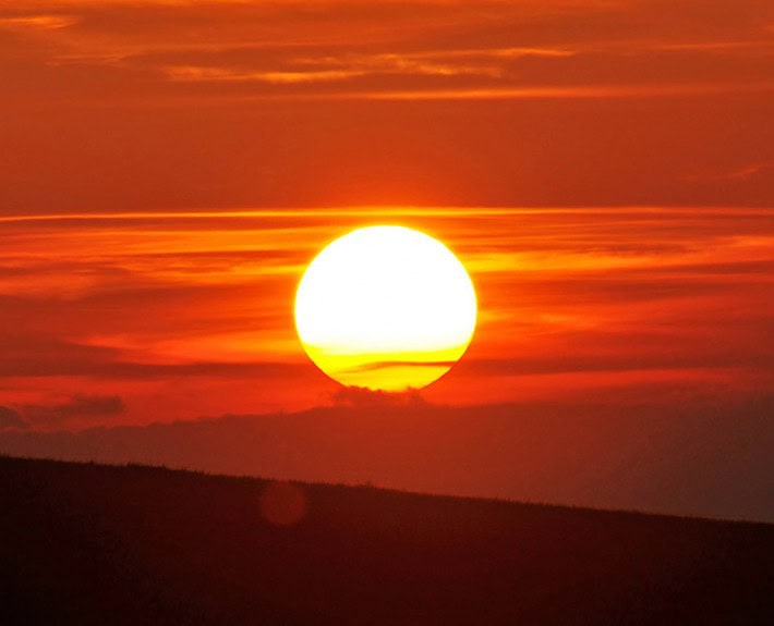 Vibrant sunset with a glowing sun over rolling hills, showcasing natural beauty.