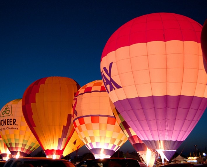 Colorful hot air balloons illuminated at night during a balloon festival.