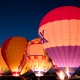 Colorful hot air balloons illuminated at night during a balloon festival.